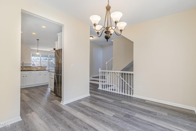 unfurnished dining area with recessed lighting, an inviting chandelier, wood finished floors, baseboards, and stairs