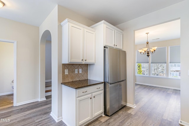 kitchen with white cabinets, light wood-type flooring, freestanding refrigerator, dark stone counters, and tasteful backsplash