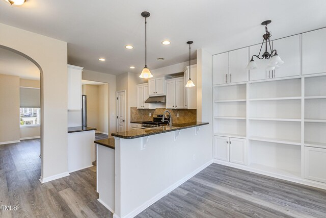 kitchen with stainless steel range, arched walkways, dark wood-type flooring, a peninsula, and white cabinetry