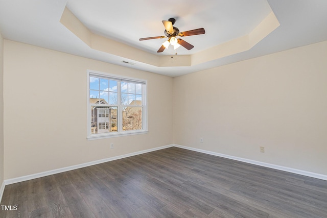 empty room featuring dark wood-type flooring, a raised ceiling, and baseboards