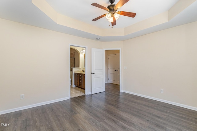 unfurnished room with dark wood-style floors, a tray ceiling, arched walkways, and baseboards