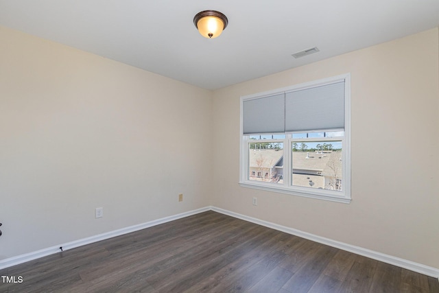 spare room with dark wood-type flooring, visible vents, and baseboards