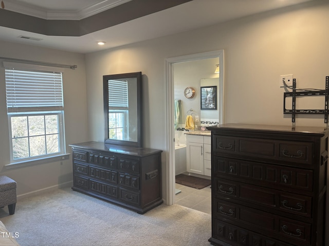 bedroom featuring light carpet, visible vents, baseboards, ensuite bath, and crown molding