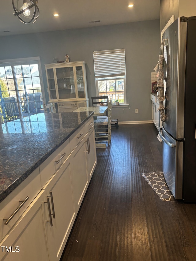 kitchen with dark wood-type flooring, baseboards, white cabinets, freestanding refrigerator, and dark stone counters