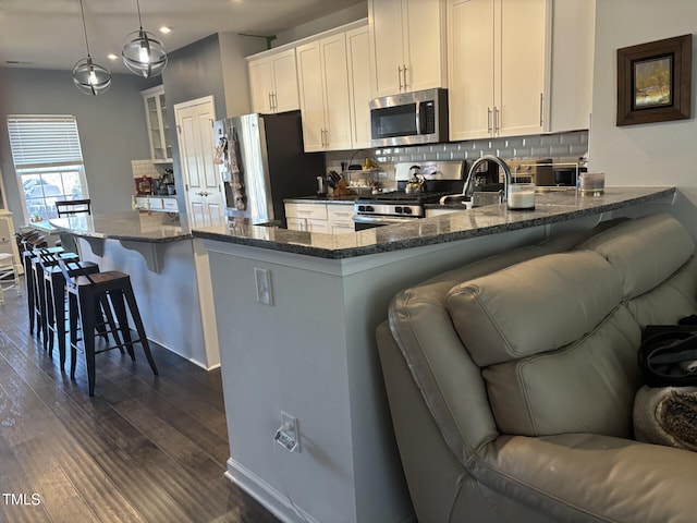 kitchen with stainless steel appliances, dark wood-style flooring, tasteful backsplash, dark stone countertops, and a kitchen bar