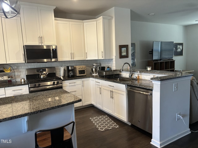 kitchen with backsplash, appliances with stainless steel finishes, white cabinetry, a sink, and a peninsula