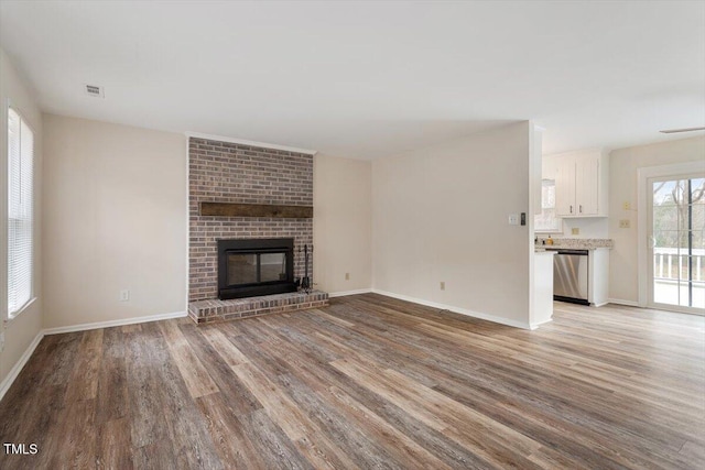 unfurnished living room featuring light wood finished floors, a brick fireplace, and baseboards