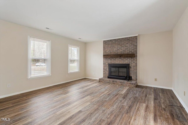 unfurnished living room featuring visible vents, baseboards, a brick fireplace, and wood finished floors