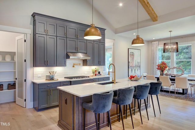 kitchen featuring light stone counters, stainless steel gas stovetop, light wood-style flooring, a sink, and under cabinet range hood