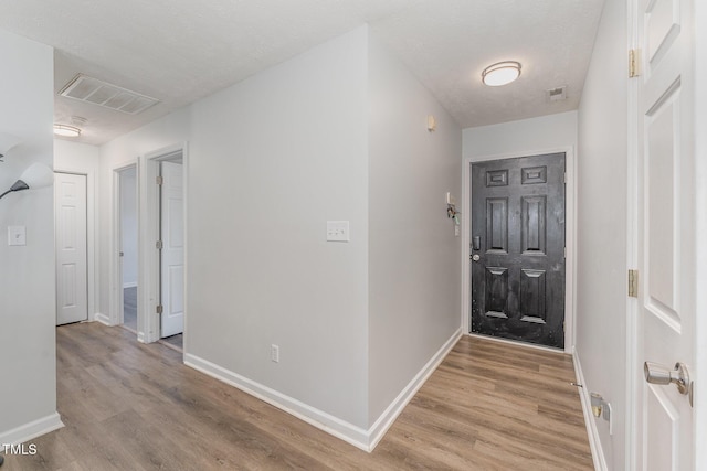 hallway with light wood-style floors, baseboards, and visible vents