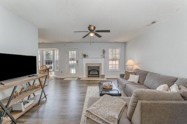 living room featuring a fireplace, wood finished floors, a ceiling fan, visible vents, and baseboards