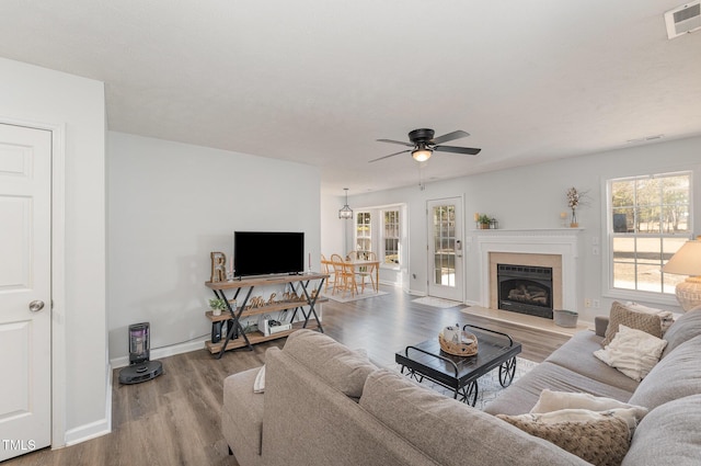 living room with a fireplace with raised hearth, ceiling fan, wood finished floors, visible vents, and baseboards