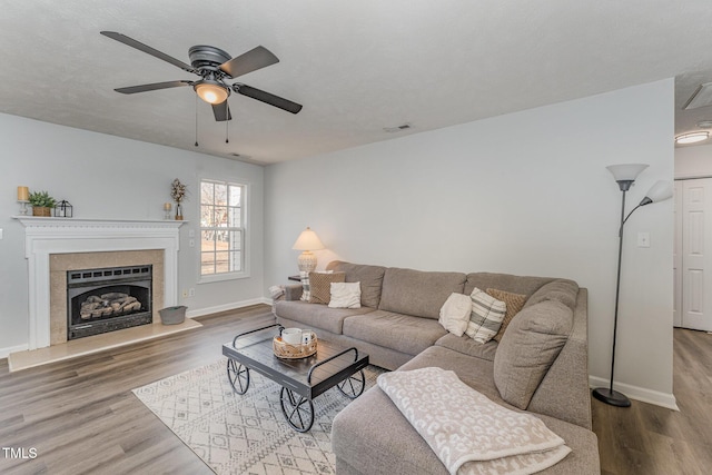 living room with baseboards, visible vents, a ceiling fan, a fireplace with raised hearth, and wood finished floors