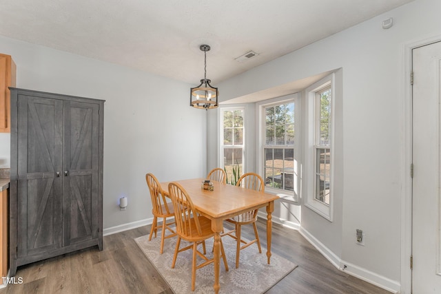 dining room with baseboards, wood finished floors, visible vents, and a notable chandelier