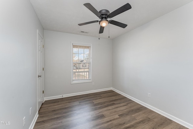 empty room with dark wood-style floors, visible vents, and baseboards