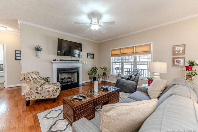 living area with a fireplace with flush hearth, crown molding, baseboards, and hardwood / wood-style floors