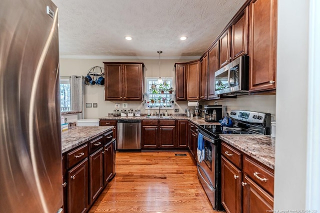 kitchen with light wood-style flooring, ornamental molding, stainless steel appliances, a textured ceiling, and pendant lighting