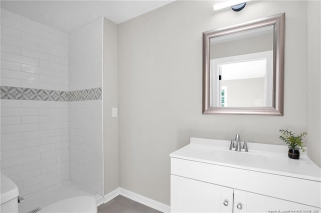 full bathroom with toilet, baseboards, tiled shower, and vanity