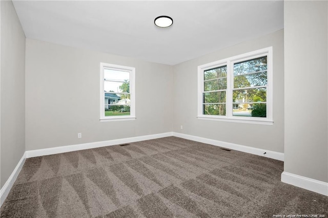 carpeted spare room featuring a healthy amount of sunlight and baseboards