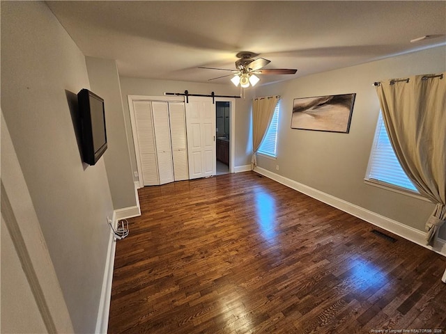 unfurnished bedroom with dark wood finished floors, visible vents, a barn door, multiple windows, and baseboards