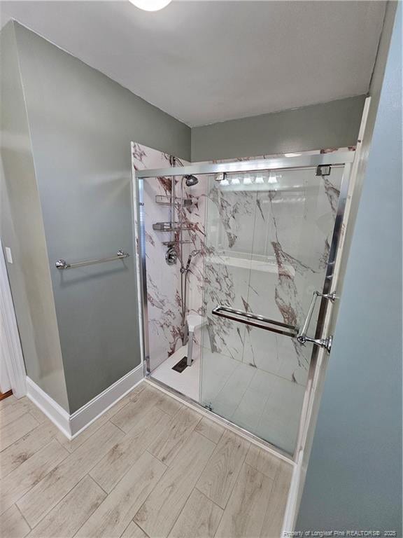 full bath featuring baseboards, a marble finish shower, and wood tiled floor