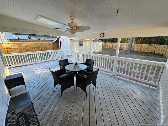 wooden deck with outdoor dining area, a storage shed, a ceiling fan, a fenced backyard, and an outdoor structure