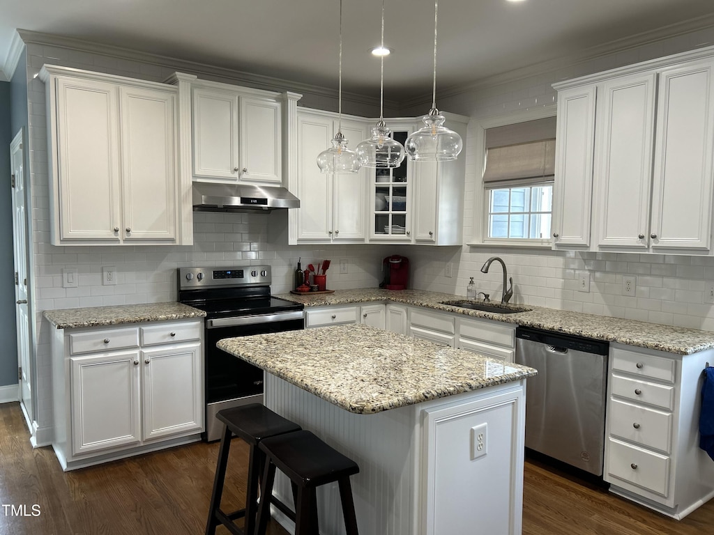 kitchen with dark wood finished floors, appliances with stainless steel finishes, under cabinet range hood, white cabinetry, and a sink