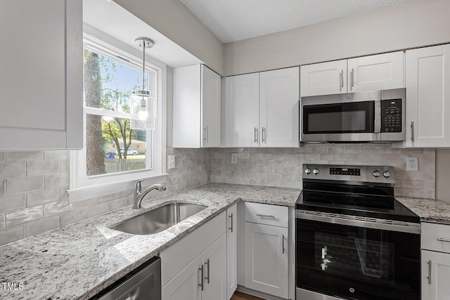 kitchen with stainless steel appliances, decorative backsplash, white cabinetry, a sink, and light stone countertops