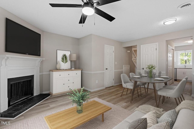 living room with visible vents, a fireplace with raised hearth, light wood finished floors, and stairs