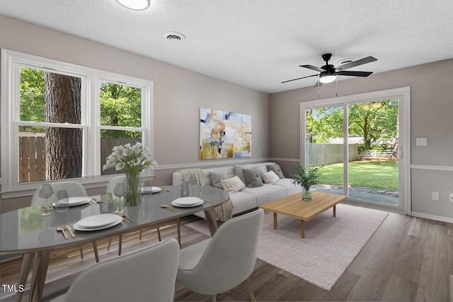 living room with a textured ceiling, wood finished floors, visible vents, and a ceiling fan