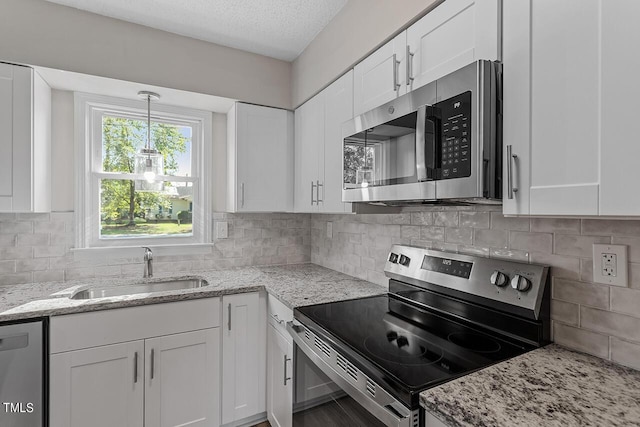 kitchen with a textured ceiling, a sink, white cabinetry, appliances with stainless steel finishes, and light stone countertops