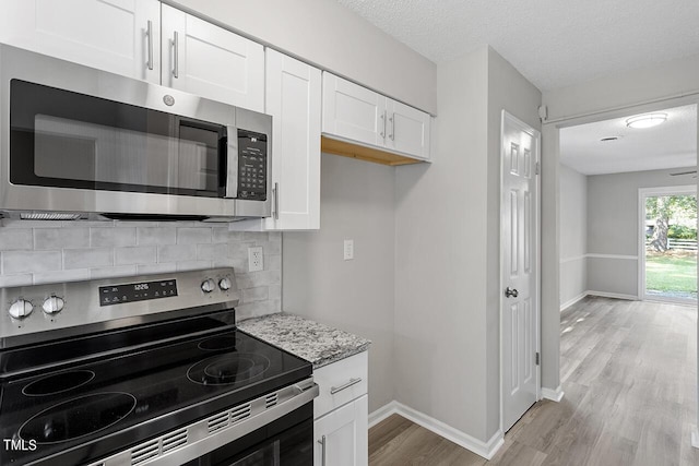 kitchen with stainless steel appliances, backsplash, light wood-style flooring, white cabinets, and light stone countertops