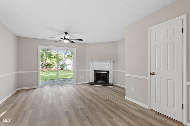 unfurnished living room with a fireplace with raised hearth, light wood finished floors, a ceiling fan, and baseboards