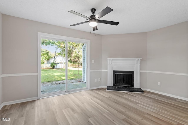 unfurnished living room with a fireplace with raised hearth, a ceiling fan, a textured ceiling, wood finished floors, and baseboards