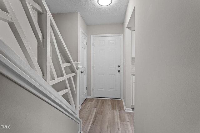 doorway with light wood-style floors and a textured ceiling