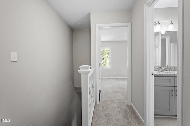 corridor with light colored carpet, a sink, a textured ceiling, an upstairs landing, and baseboards