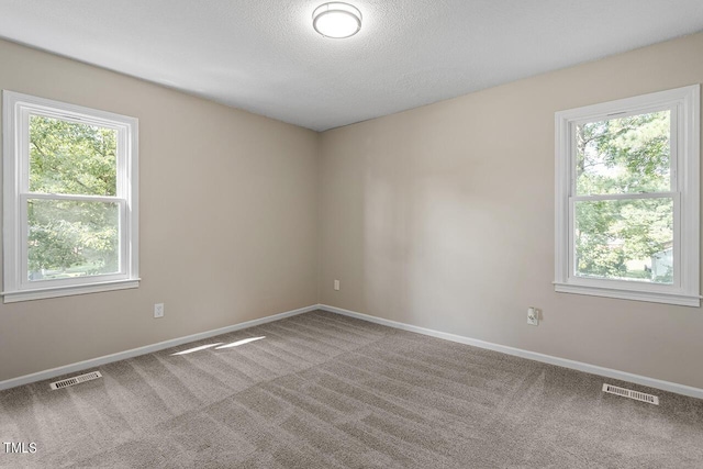 unfurnished room featuring a textured ceiling, carpet, visible vents, and baseboards