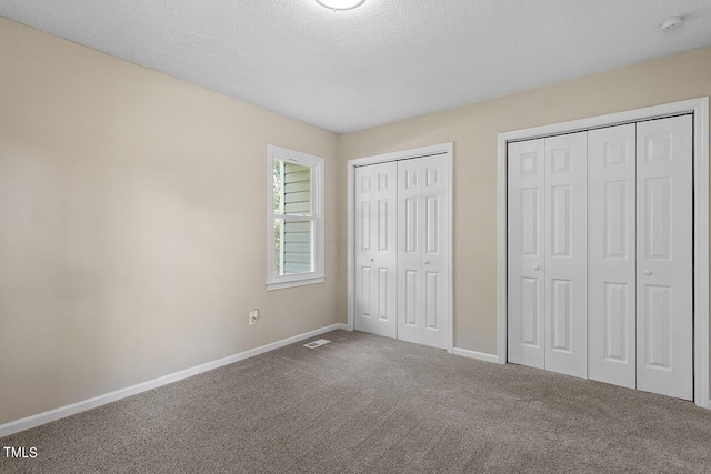 unfurnished bedroom with visible vents, baseboards, a textured ceiling, carpet flooring, and multiple closets