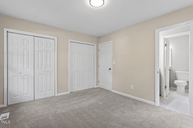 unfurnished bedroom featuring baseboards, visible vents, a textured ceiling, carpet floors, and multiple closets