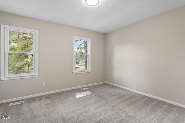 carpeted spare room with a textured ceiling, visible vents, and baseboards