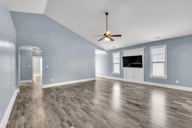 unfurnished living room with arched walkways, plenty of natural light, ceiling fan, and dark wood-style flooring