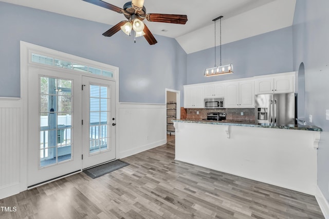 kitchen featuring dark stone countertops, a wainscoted wall, light wood finished floors, appliances with stainless steel finishes, and white cabinetry