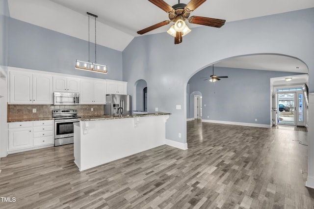 kitchen with dark stone counters, arched walkways, appliances with stainless steel finishes, white cabinetry, and open floor plan