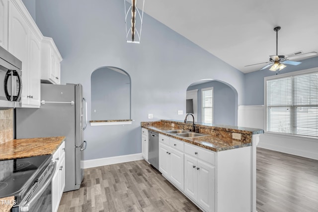 kitchen featuring appliances with stainless steel finishes, a peninsula, light wood-style floors, white cabinetry, and a sink