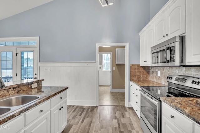 kitchen with wainscoting, appliances with stainless steel finishes, light wood-style floors, white cabinets, and a sink