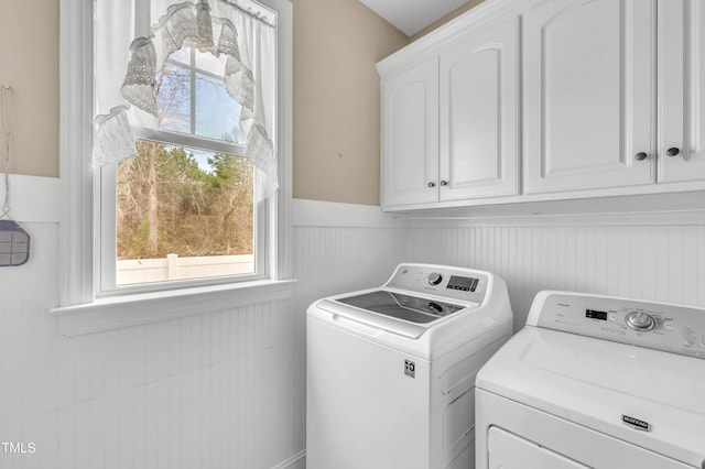 laundry room featuring washing machine and clothes dryer, a wainscoted wall, and cabinet space