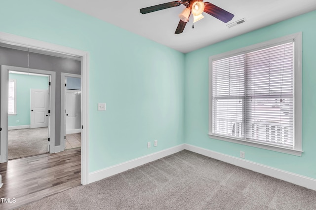 carpeted spare room featuring a ceiling fan, plenty of natural light, baseboards, and visible vents