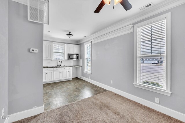 kitchen featuring ornamental molding, a sink, stainless steel microwave, white cabinetry, and carpet floors