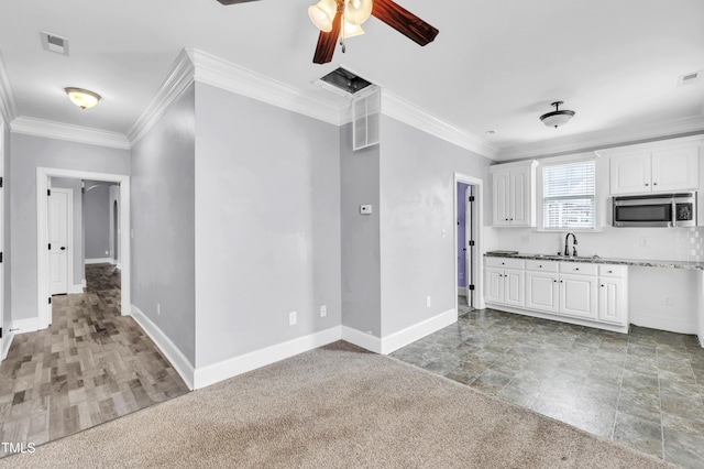 kitchen featuring ornamental molding, a sink, stainless steel microwave, white cabinets, and baseboards