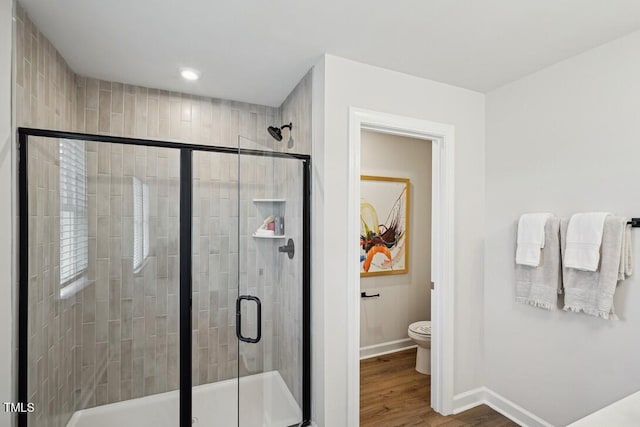 full bathroom with a stall shower, wood finished floors, toilet, and baseboards